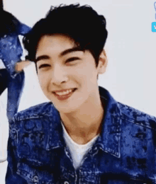 a young man in a denim jacket is smiling and looking at the camera .