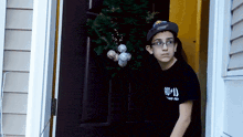 a boy wearing glasses and a black shirt with the letter u on it stands in a doorway
