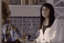 two women are standing next to each other in a kitchen and talking to each other .