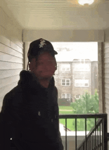 a man wearing a hat and headphones is standing on a balcony looking out over a building .