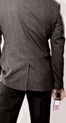 the back of a man in a suit is shown holding a bottle of perfume .