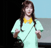 a woman in a green shirt with a yellow collar is holding a heart shaped bag