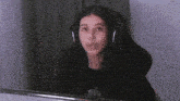 a woman wearing headphones and a black shirt is sitting in front of a computer screen .