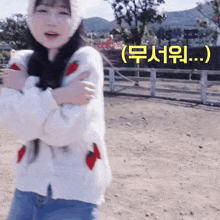 a girl wearing a white sweater with strawberries on it is standing in a dirt field