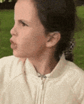 a little girl in a white jacket is making a face