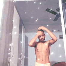 a shirtless man is standing in front of a mirror with a ceiling fan in the background