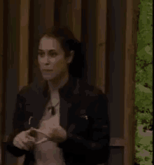a woman in a black jacket is standing in front of a wooden fence holding a cell phone .