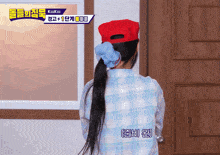 a woman wearing a red hat and a blue scrunchie stands in front of a wooden door