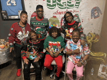 a group of people wearing ugly sweaters pose in front of a ugly sweaters banner