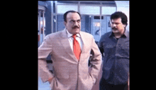 a man in a suit and tie is standing next to another man in a black shirt .