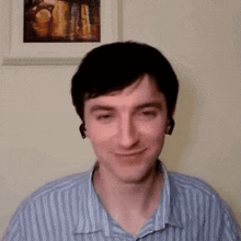 a man wearing headphones and a striped shirt is smiling in front of a painting on the wall .