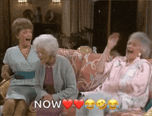 three elderly women are sitting on a couch laughing and holding hands .