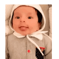 a baby wearing a white hat and a gray shirt is sticking his tongue out .