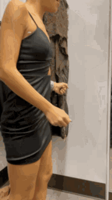a woman in a black dress is standing in front of a mirror in a dressing room