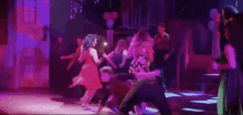 a group of people are dancing on a stage in a dark room with balloons in the background .