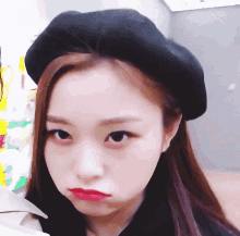 a woman wearing a black hat and red lipstick looks at the camera