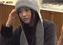 a woman wearing a hooded scarf and a sweater is sitting at a table .
