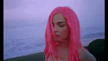 a woman with bright pink hair is sitting on a beach .