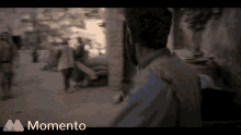 a man is walking down a street with a momento logo behind him