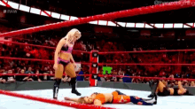 a woman is standing in a wrestling ring next to a woman laying on the ground .