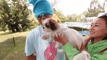 a man wearing a blue beanie is holding a small white dog