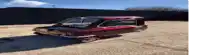 a red car is parked on a gravel road next to a fence .