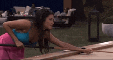 a woman in a blue tank top and pink skirt is playing shuffleboard .