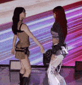 two women are dancing on a stage in front of a purple background