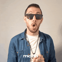a man wearing sunglasses and a denim shirt has the word mcdh on his shirt