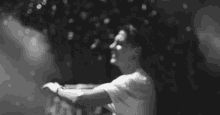 a black and white photo of a man standing in front of a wall with confetti falling on him .