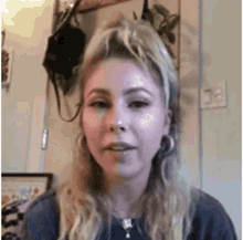 a woman with blonde hair and hoop earrings is sitting in front of a mirror in a room .