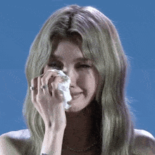 a woman is crying while holding a tissue to her face .