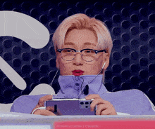 a man wearing glasses and headphones is playing a video game on a cell phone .