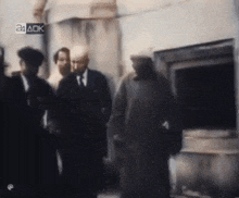 a group of men are standing in front of a building with a 24 ack logo on the bottom right