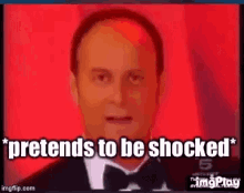 a bald man in a tuxedo and bow tie is talking and pretending to be shocked .