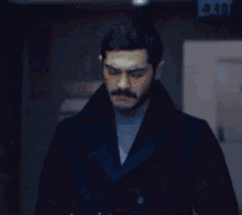 a man in a black coat stands in front of a blue exit sign