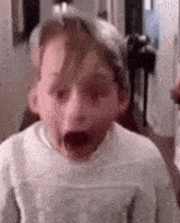 a young boy is making a funny face with his mouth open and his eyes closed .