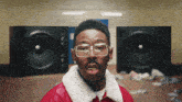 a man wearing glasses and a red jacket stands in front of a pair of speakers