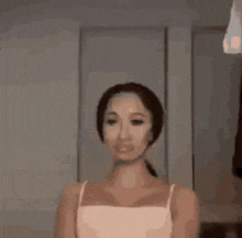 a woman in a white tank top is standing in front of a mirror in a room .