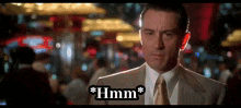 a man in a suit and tie is standing in front of a sign that says " hmm "