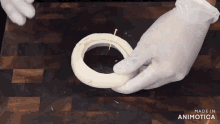 a person wearing white gloves is holding a ring on a wooden cutting board that says made in animatica