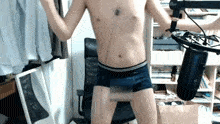 a shirtless man stands in front of a microphone in a room