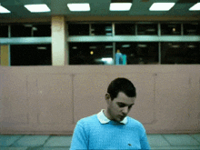 a man in a blue sweater is standing in front of a wall