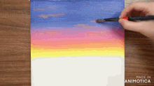 a person is painting a sunset with a brush on a canvas