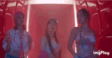 three women are standing next to each other in front of a red wall in a room .