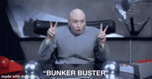dr. evil is sitting at a desk giving a peace sign .