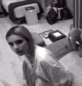 a black and white photo of a woman sitting on a bed in a room .