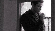 a black and white photo of a man looking out of a window .