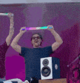 a man wearing sunglasses is holding a light up stick over his head while standing in front of a speaker