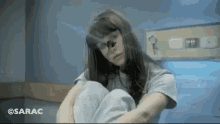 a woman in a hospital gown is sitting on the floor with her arms around her knees .